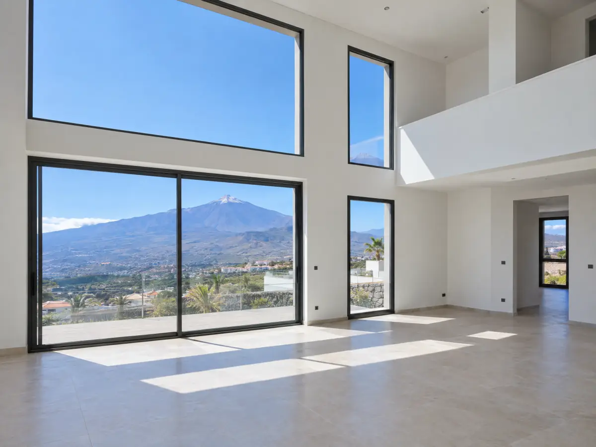 Salón a doble altura de una vivienda de obra nueva con ventanales hacia el Teide