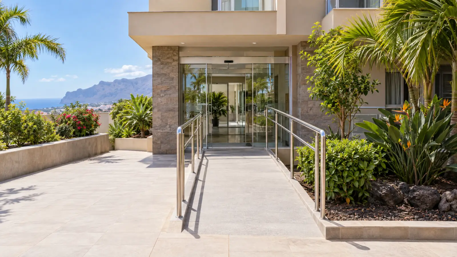 Entrada de un edificio en Tenerife con rampa accesible, pasamanos y puerta automática (recreación ilustrativa)